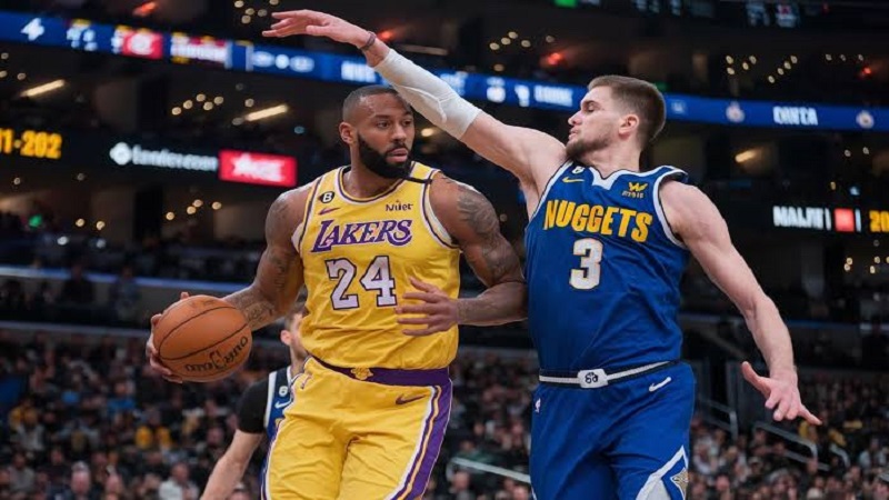 Los Angeles Lakers player dribbling while being closely guarded by a Denver Nuggets player during an NBA game.